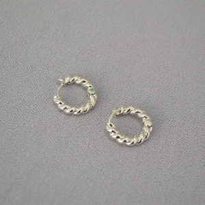Détail de boucles d'oreilles créoles torsadées argentées sur fond de tissu gris texturé