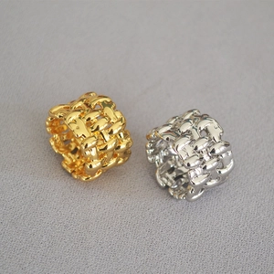 Detailed view of woven mesh rings in polished gold and silver finishes on gray fabric