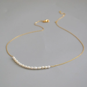 Détail d'un collier chaîne dorée avec une rangée de perles de riz d'eau douce blanches