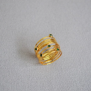 Detail of golden multilayer wire ring with green gemstones on gray fabric background