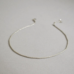 Macro shot of minimalist silver twist chain necklace on textured grey fabric background