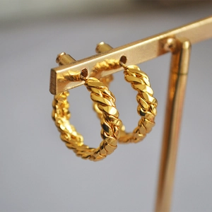 Macro detail of gold plated twisted rope hoop earrings with polished metallic texture