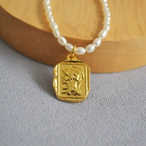 Macro detail of French retro gold square coin pendant with Roman relief on pearl necklace