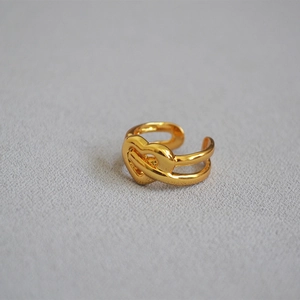 Detail of gold-plated brass knot ring with heart design on grey textured fabric