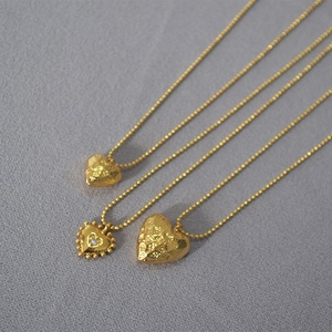 Detailed macro view of three textured gold heart pendants on matching ball chains