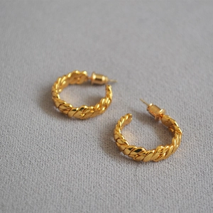Detailed view of woven braided gold hoop earrings with retro twisted metal texture