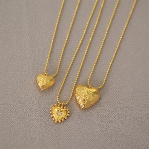 Macro shot of gold-plated heart pendant necklaces with textured surfaces and zircon details