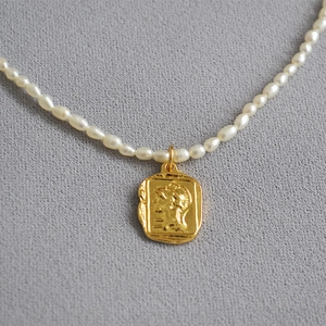 Close-up of pearl necklace with gold rectangular coin pendant featuring relief portrait
