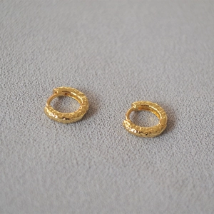 Macro shot of gold hoop earrings with hammered texture on a neutral fabric background