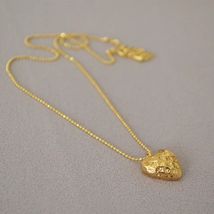 Detail of gold heart pendant with hammered texture on elegant beaded ball chain necklace
