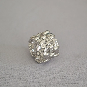 Macro view of wide silver-plated ring with woven grid texture and artistic metal details