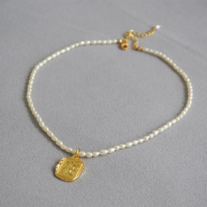 Detailed macro view of square gold coin pendant and freshwater rice pearls necklace