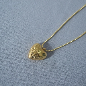Minimalist hammered texture heart pendant necklace with gold bean chain on blue background