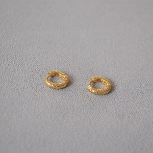 Detailed view of golden hoop earrings with handcrafted hammered texture on grey fabric