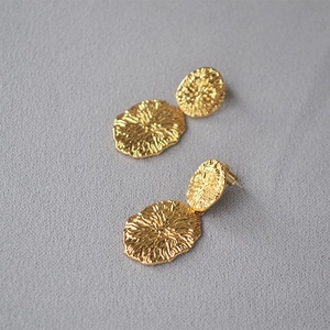 Golden irregular textured oval drop earrings with detailed sunburst rays on grey fabric