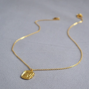 Close-up of a vintage square gold coin pendant with Roman relief and fine chain links