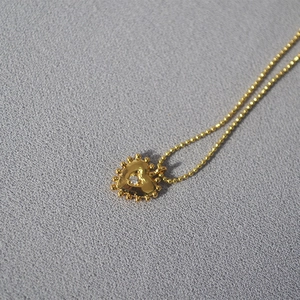 Detailed macro view of a heart pendant necklace with gold beaded edges and center zircon