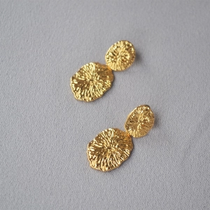 Macro shot of gold textured metal earrings with handmade irregular engraved patterns