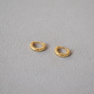 Macro shot of gold hoop earrings featuring a hammered texture on a textured grey surface