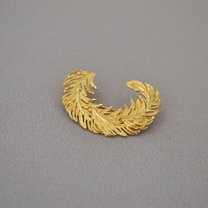 Golden phoenix wing feather brooch with 3D layers on textured grey fabric
