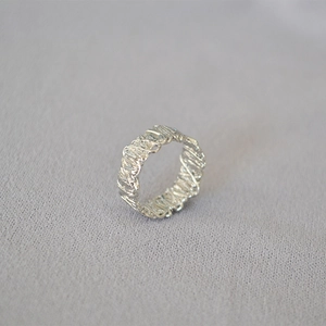 Macro view of minimalist silver ring with irregular twisted texture and molten metal finish