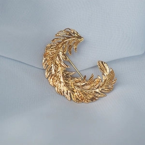 Macro shot of golden feather brooch with intricate brushed texture on blue fabric