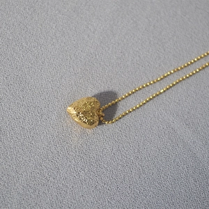 Detail of gold heart pendant with hammered texture and delicate beaded chain