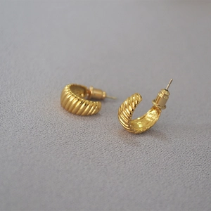 Macro detail of gold-plated croissant earrings showing textured ridges and silver needles