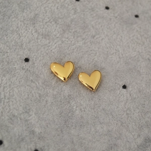 Macro shot of polished heart stud earrings in gold finish on grey velvet background