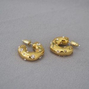 Detail of chunky gold C-shaped hoop earrings with sparkling rhinestones on grey fabric