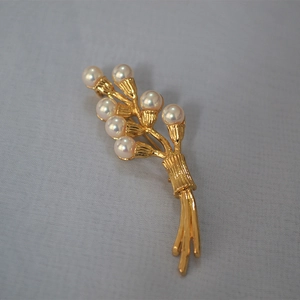 Macro detail of golden wheat brooch with glossy pearls on textured grey fabric