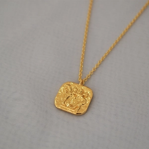 Gros plan du relief d'ange double face sur un collier en laiton plaqué or carré