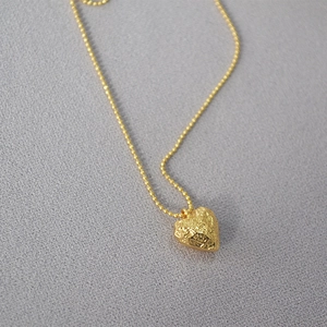 Textured gold heart pendant necklace with elegant ball chain for women on grey fabric
