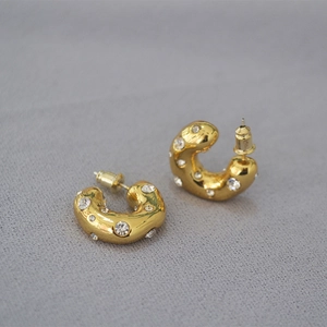 Close-up of chunky gold-plated C-shaped earrings with sparkling rhinestone inlay details