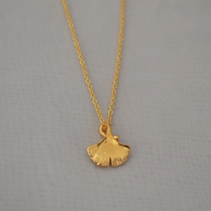 Elegant gold ginkgo leaf pendant necklace with detailed vein texture on gray fabric