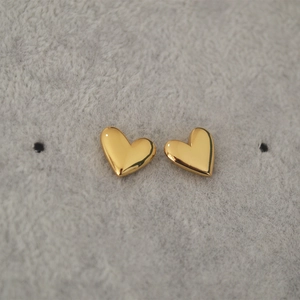 Polished gold heart stud earrings on grey velvet display with reflective mirror finish
