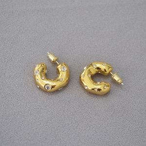 Macro shot of chunky gold C-shaped hoop earrings with sparkling cubic zirconia on fabric