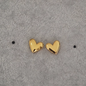 Macro detail of high-polished gold-plated heart stud earrings on soft grey texture
