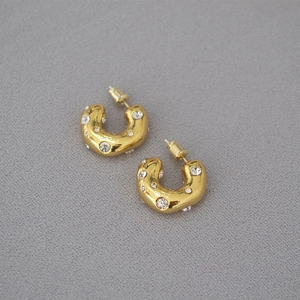 Macro detail of chunky gold C-shaped hoop earrings with sparkling inset crystals