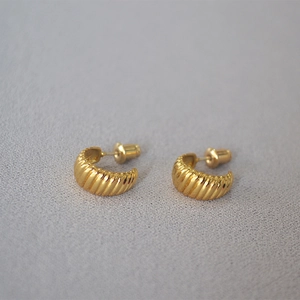 Macro detail of gold plated croissant stud earrings with elegant radial textured patterns