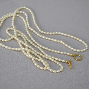 Collier élégant en perles de riz avec fermoir OT doré sur un tissu gris texturé