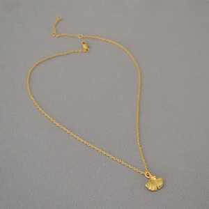 Minimalist gold-plated ginkgo leaf pendant necklace with delicate O-chain on grey fabric