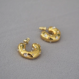 Close-up of golden chunky C-shaped hoop earrings with sparkling white cubic zirconia