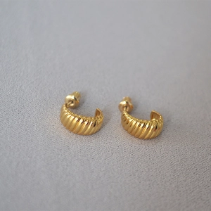 Close-up of gold croissant stud earrings with ribbed texture on gray background