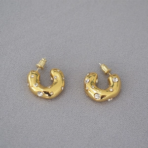 Macro detail of chunky gold C-shaped hoop earrings with irregular sparkling crystals