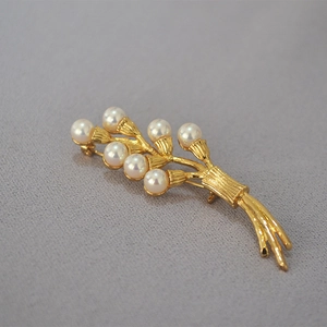 Macro detail of golden flower brooch featuring lustrous pearls and brushed metal texture