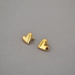 Macro shot of polished gold heart stud earrings on a textured grey fabric background