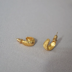 Macro detail of gold croissant hoop earrings showing the textured spiral pattern and finish