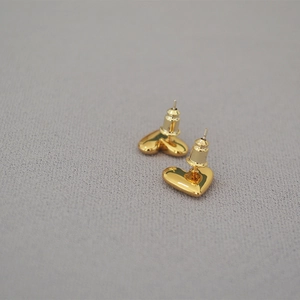 Minimalist heart-shaped polished gold-plated stud earrings on a textured fabric backdrop