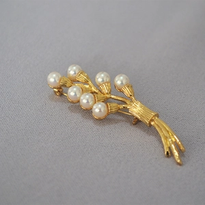 Detailed close-up of golden floral brooch with seven white pearls on grey fabric